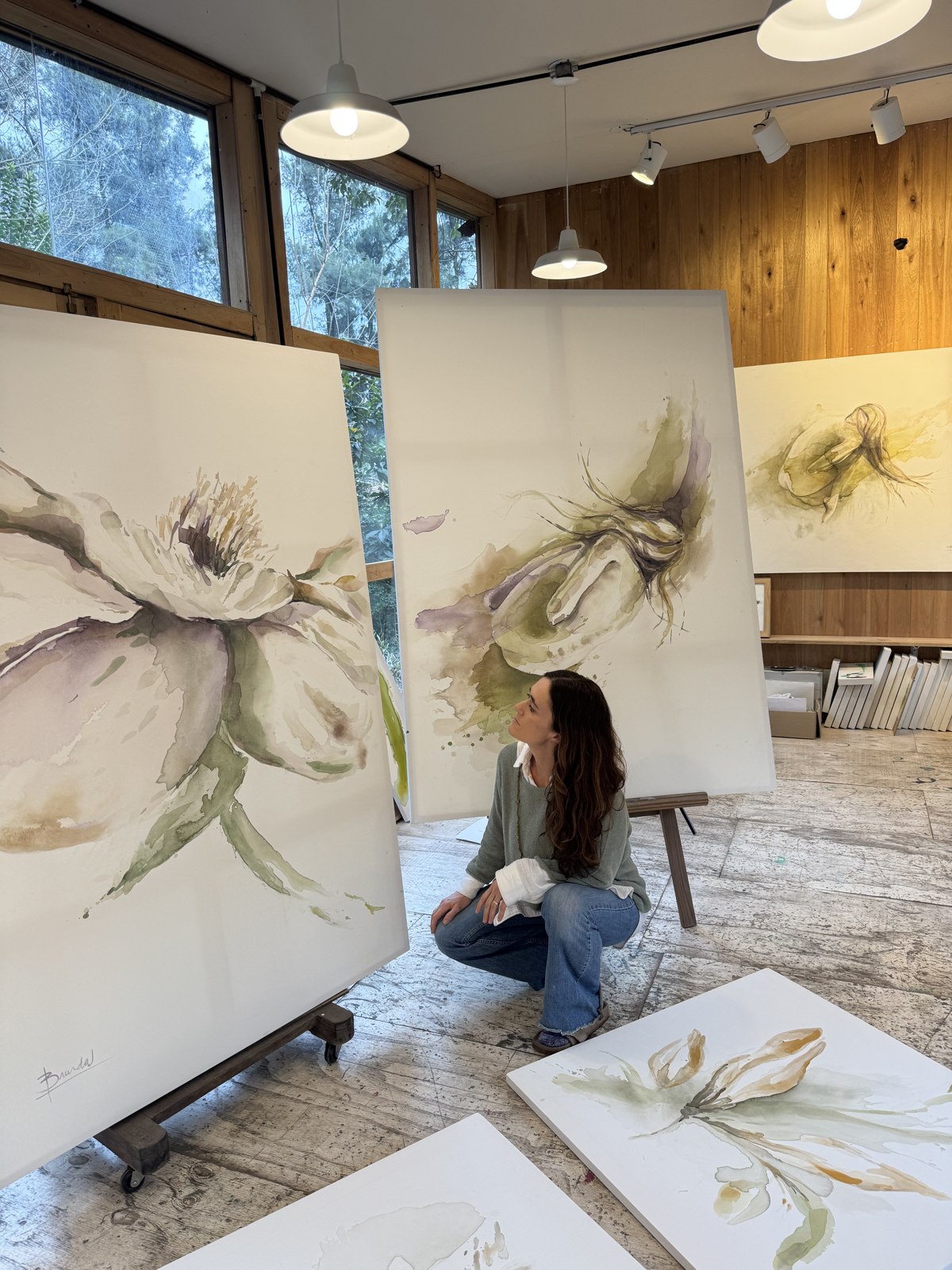 Brenda Rodríguez in her studio with two large white flower canvases
