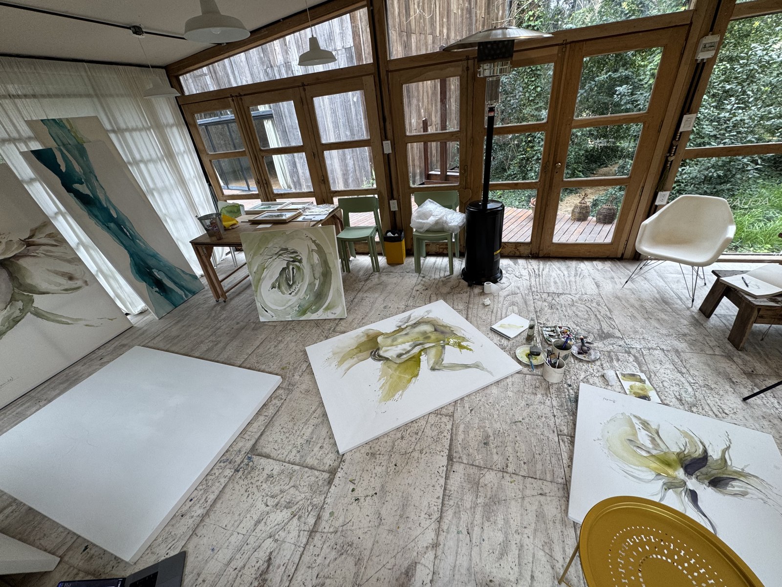 Wide view of Brenda Rodríguez's atelier with canvases leaning and lying across the floor, garden visible through the glass doors