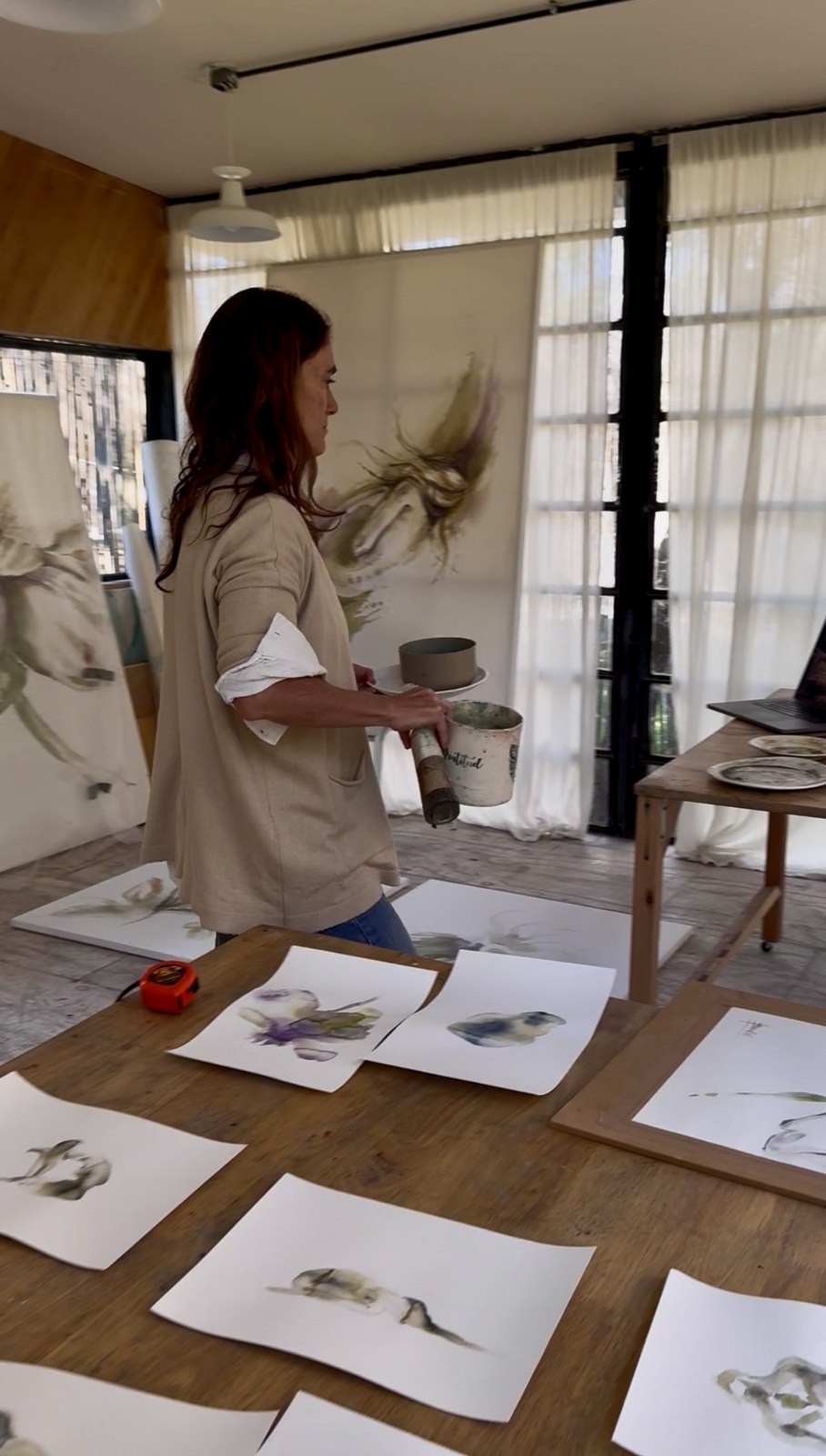 Brenda Rodríguez standing at a long wooden table covered with her works on paper