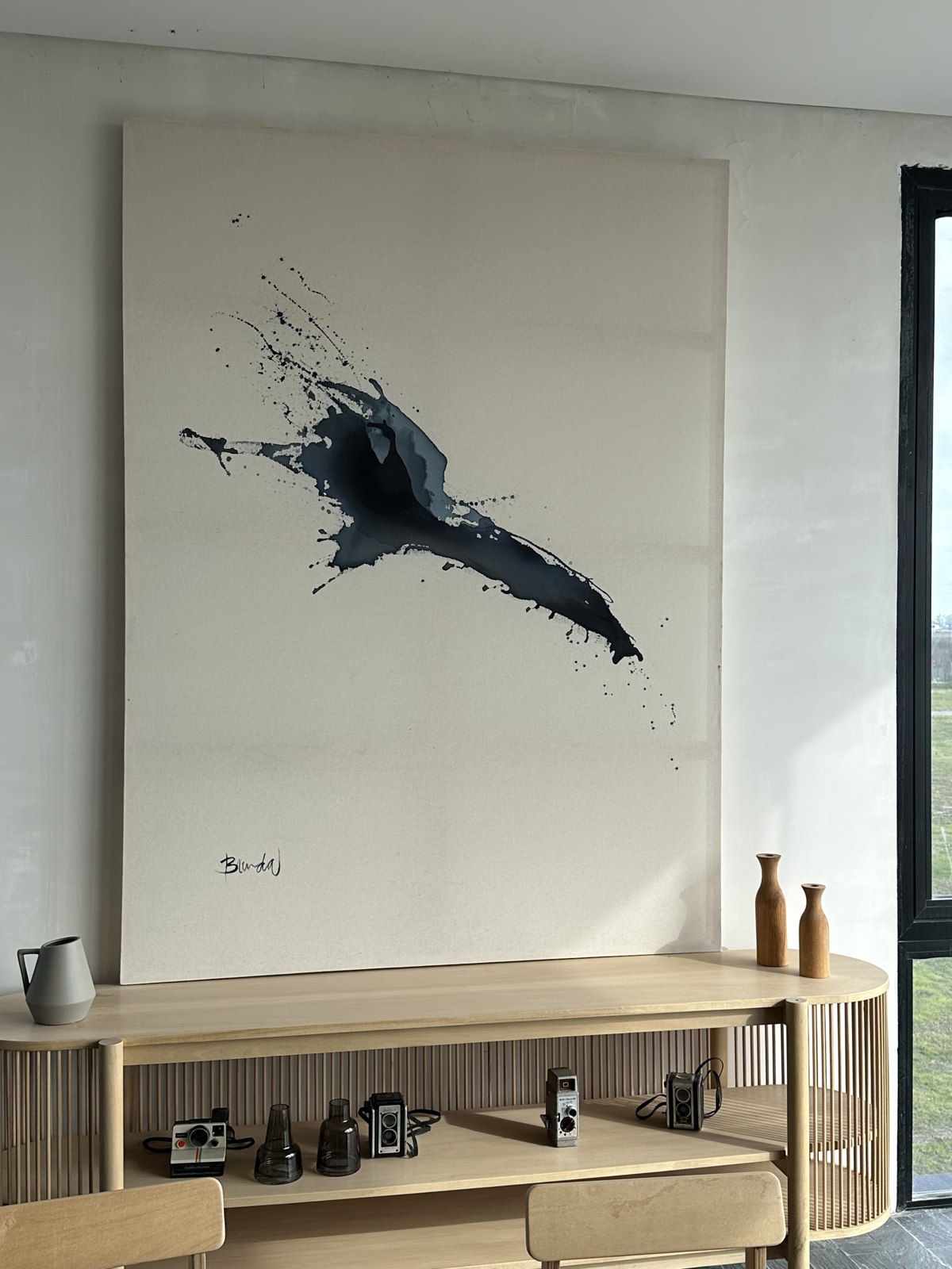 Large dark ink splash canvas by Brenda Rodríguez hanging above a wooden sideboard