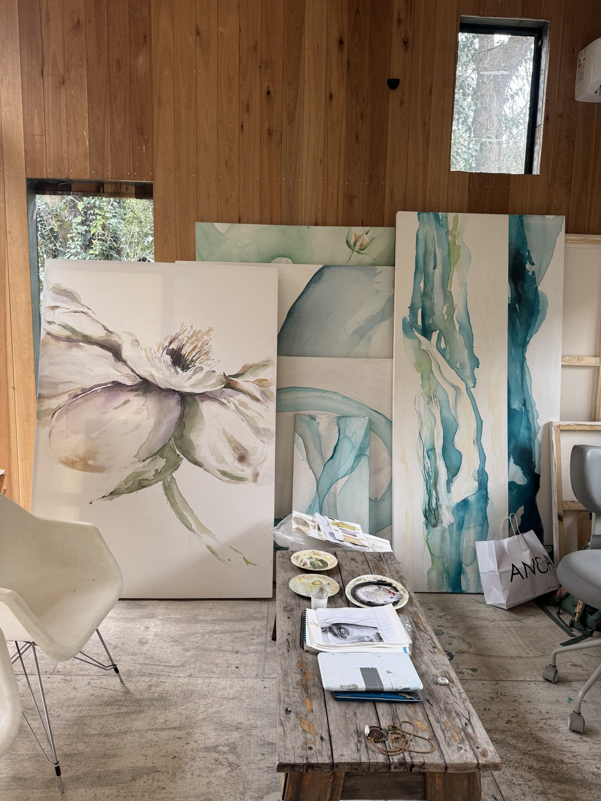 Studio view with teal water paintings by Brenda Rodríguez leaning against a wood wall